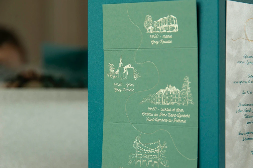 illustrations de bâtiments et arbres imprimées en dorure sur papier de création vert sauge fixé sur une pochette bleu paon