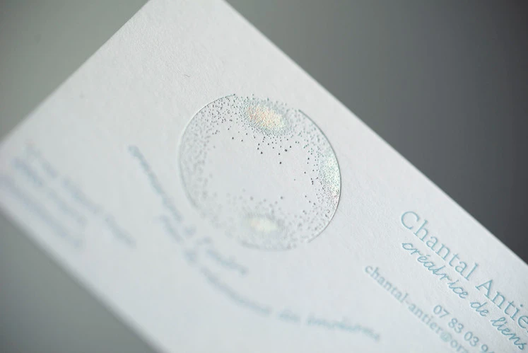 détail de texte de carte de visite en impression typographique couleur bleu clair sur papier texturé blanc et marquage à chaud holographique en forme de bulle