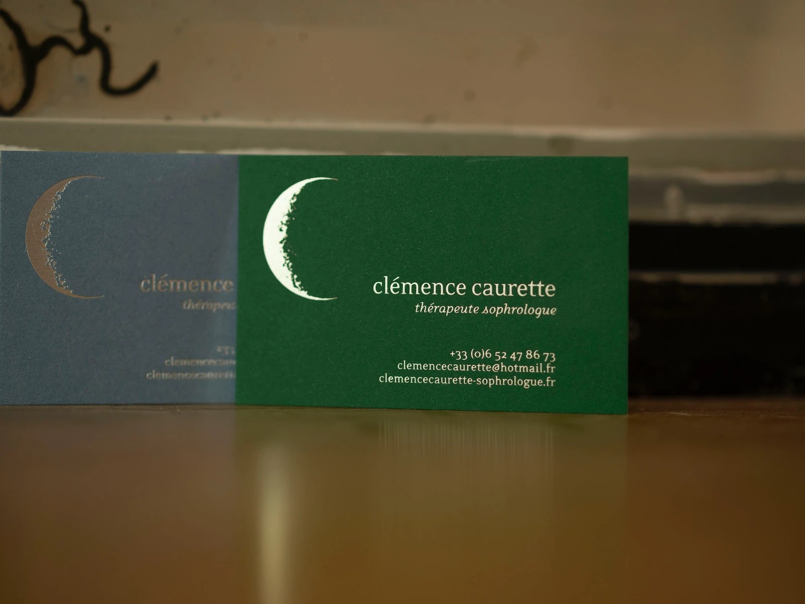 deux cartes de visite en marquage à chaud argent sur papier bleu gris texturé et or pâle sur papier vert devant miroir