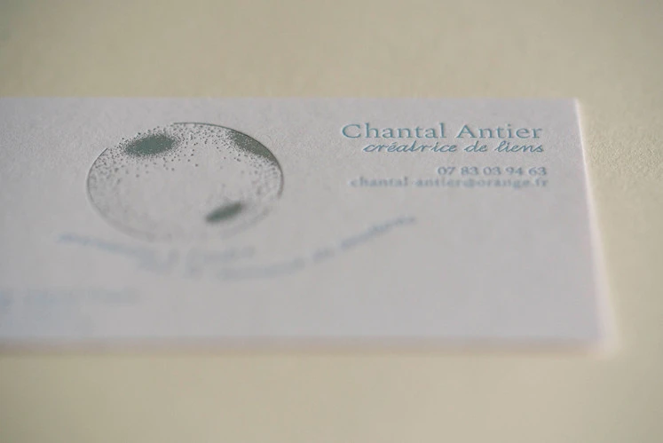 détail de texte de carte de visite en impression typographique couleur bleu clair sur papier texturé blanc et marquage à chaud holographique en forme de bulle